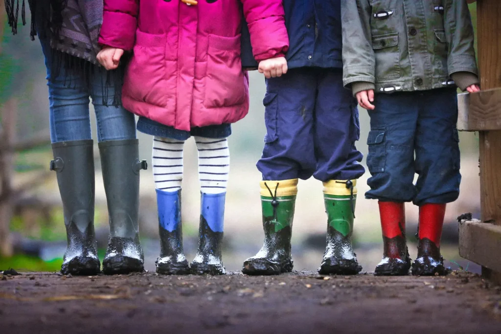 Four children pictured from the chest down, wearing muddy boots and holding hands